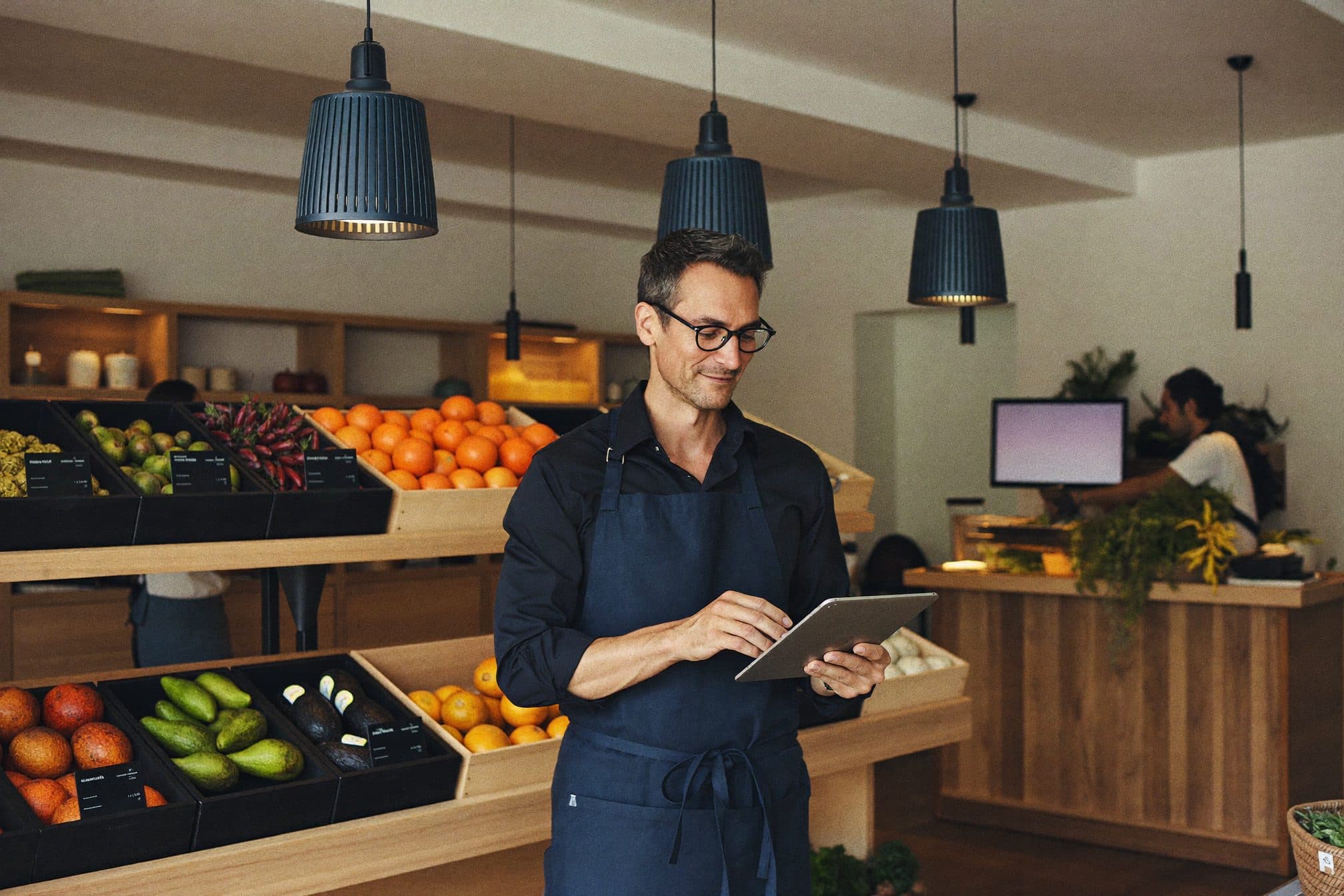 El encargado de un mercado gourmet revisa el stock en una tablet, junto a la verdulería.